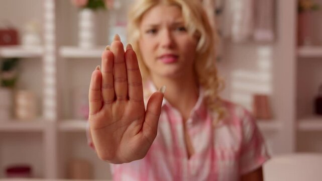 Serious Caucasian teen girl showing stop hand in pink bathroom looking at camera refusing blonde woman female with no gesture protect boundary arm distance reject deny negative emotion at home bath