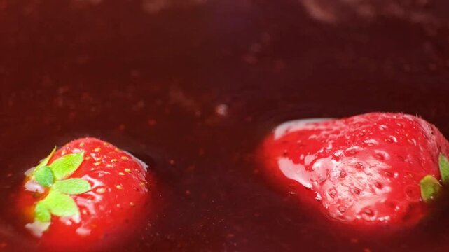 Slow motion close up of fresh strawberries falling into sweet red sauce