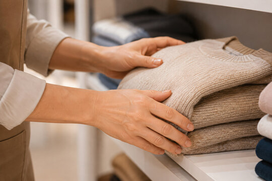 Close-up of a shopper selecting folded knit sweaters on a shelf in a modern clothing store
