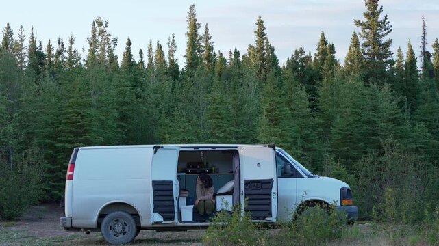 Woman sitting in camper van exploring remote Alaska wilderness during a nomadic journey