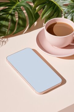 Smartphone mockup with pink coffee cup and monstera leaves on pastel surface