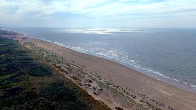 Aerial view video clip of Katwijk aan Zee wide sandy beach, coastal sand dunes landscape, sunlight reflection on sea, and North Sea horizon in South Holland, Netherlands