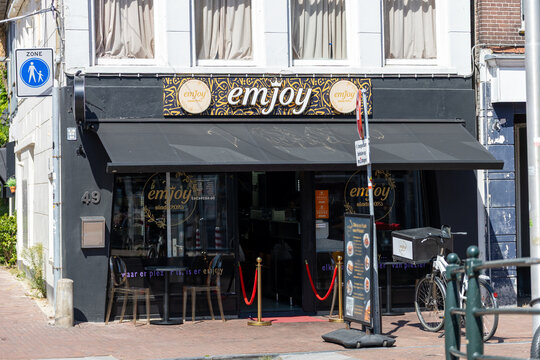 Sneek, Netherlands - August 9, 2026: Exterior view of Emjoy restaurant in Sneek, showing the black storefront, signage, entrance, menu board, bicycle and pedestrian zone sign on a sunny city street.