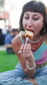 Vertical shot. A young woman eats pide at a cozy street food festival, sampling various street foods. Close-up of the food. Summer vibes.