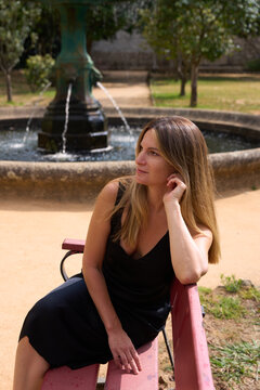 Woman Sitting on a Bench by a Fountain in a Park