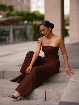 Asian Woman Sitting On Stairs Wearing Brown Outfit