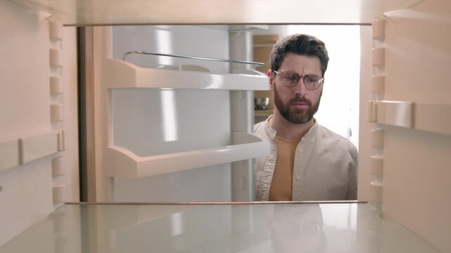 Point of view inside refrigerator hungry Caucasian man sad frustrated with empty fridge in kitchen disappointed male bachelor unemployment crisis no food without products food delivery grocery service