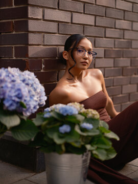 Asian Woman Leaning Brick Wall Near Hydrangeas Looking Camera