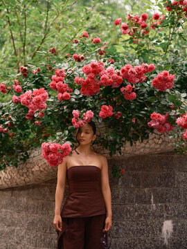 Asian Woman Standing Eyes Closed Under Blooming Pink Roses Wall