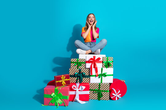 Young woman sits on colorful gift tower against a bright blue background smiling and festive