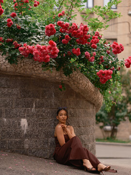 Asian Woman Sitting Near Stone Wall Under Blooming Roses