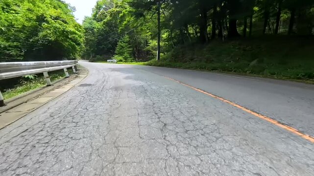 Motorcycle POV riding a cracked forest road along a guardrail
