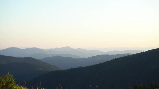 Mountain landscape with silhouettes of peaks in soft sun rays, green and blue tones

