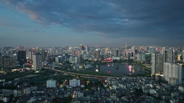 Aerial cityscape of Cau Giay District, Hanoi, featuring Ring Road 3, urban development, high-rise architecture, a lake, and illuminated streets beneath a dramatic evening sky.