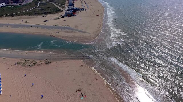 Aerial view video clip of Katwijk aan Zee river mouth, Oude Rijn outlet entering North Sea, beach cabins, sand dunes, and sea surface sunlight glint in South Holland, Netherlands