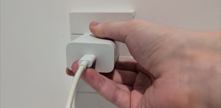 Hand plugging type-A phone charger block into a universal Type A and C electrical outlet, adjusting a USB Type-C cable, and unplugging. Power supply, energy consumption, and daily routine concept.