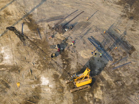 Aerial view of the Waste to Energy Facility Construction Project with a yellow crawler crane, workers, and steel rebar on the dirt site in Kecamatan Denpasar Selatan, Bali, Indonesia.
