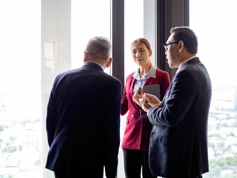 Three businesspeople standing by an office window discussing strategy, teamwork, leadership, communication, planning, collaboration, management, and professional decisions