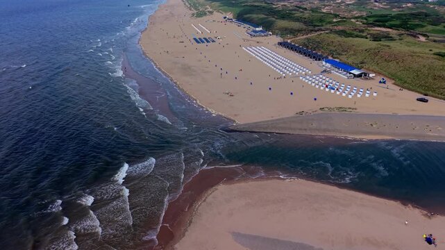 Aerial view video clip of Katwijk aan Zee river mouth, Oude Rijn outlet meeting North Sea, beach resort cabins, beach houses, sand dunes, and sea waves in South Holland, Netherlands