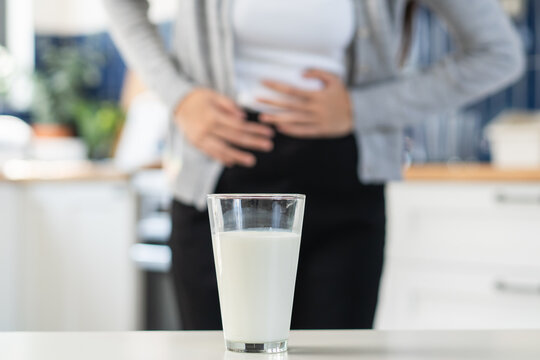 Lactose intolerant, Close-up hands of person holding a glass of milk and feeling stomach pain.