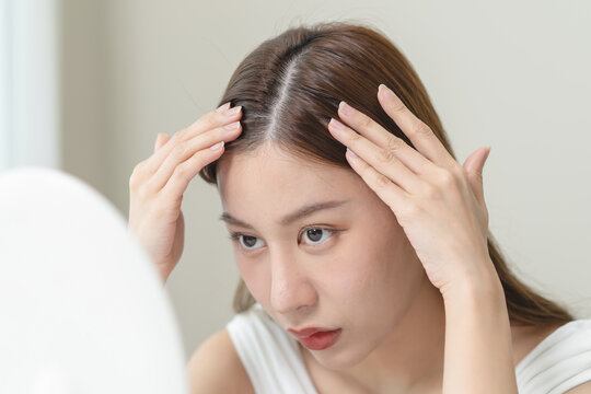 problem hair fall asian young woman, girl worry about balding, looking at scalp in mirror, hand in break into front hair loss, thin problem.