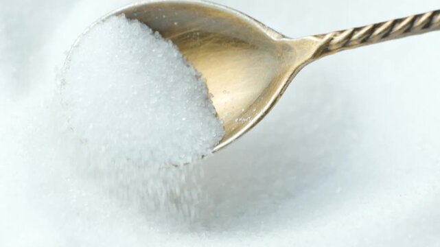 White salt crystals pouring out of a spoon in slow motion