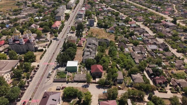 Aerial drone flight over Hincesti, Moldova, showing an Orthodox church with golden domes, a large abandoned and deteriorating building, main road, residential houses and surrounding urban landscape on