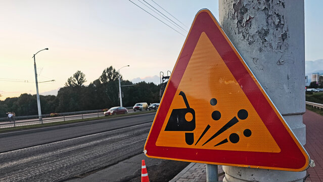 Road sign warning of loose chippings and flying stones along a street with cars passing by, indicating ongoing road construction
