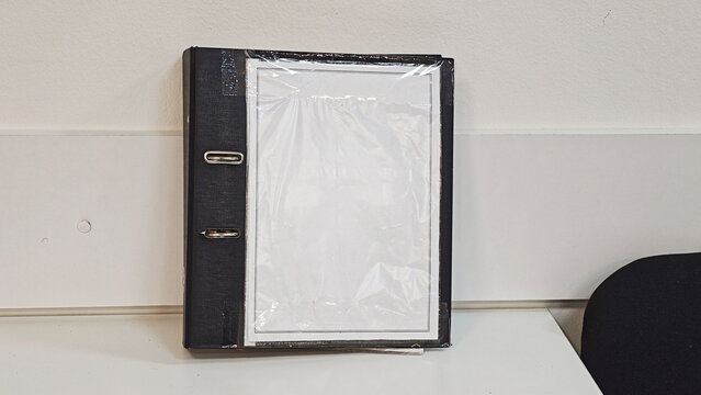 Black ring binder standing on a white table, providing a blank customizable label for documents and office organization