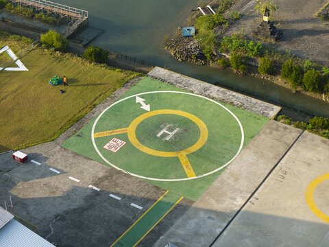Aerial view of a helipad with green and yellow markings situated near a waterway and grassy area in Kecamatan Denpasar Selatan, Bali, Indonesia.