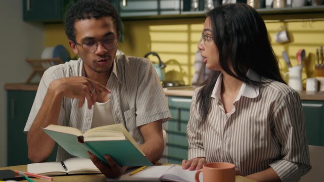 African American guy and Indian girl arguing while studying at home kitchen college students discussing homework exam conflict misunderstanding reading book together frustrated gen z friends quarrel