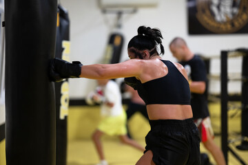 Fototapeta premium Female Boxer Training on Heavy Bag in Gym During Intense Fitness Workout Session