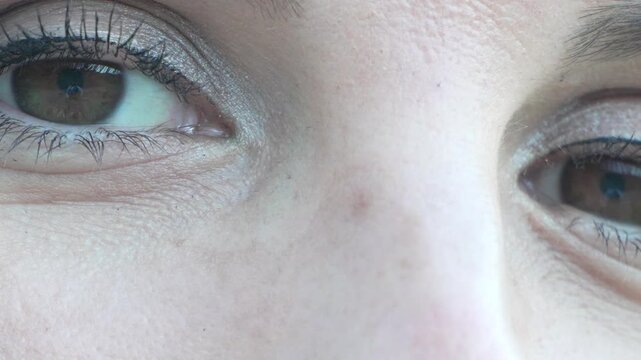 Winged eyeliner look displays soft brown iris as a woman observes her reflection. Macro tracking shot moves across expressive facial features.