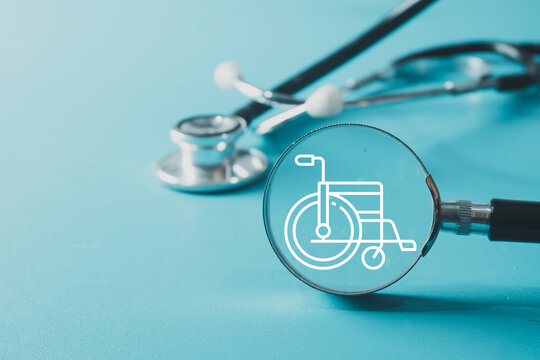 Close up of a magnifying glass focusing on a digital wheelchair icon next to a medical stethoscope on a blue background. Concept of disability healthcare, rehabilitation, and accessibility.