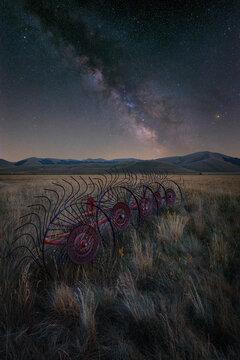 View of a rusty hay rake in a field under the Milky Way at night in Castelluccio, Umbria, Italy.