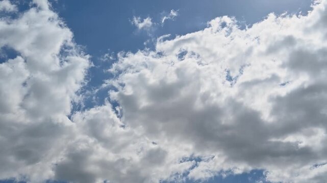 Fluffy cumulus and stratocumulus clouds moving rapidly across a blue sky with sunlight peeking through during sunny day. 4K timelapse background footage