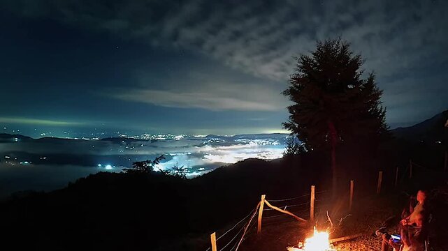 campfire under starry night with city lights view from mountain