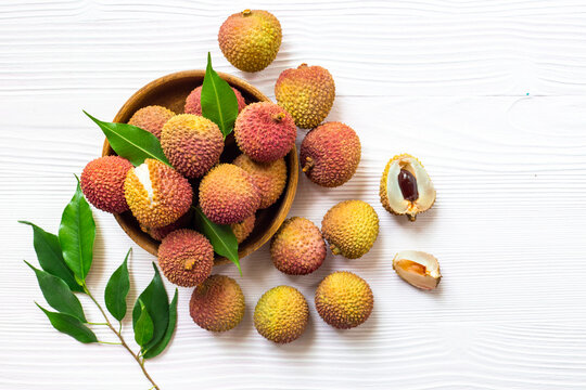 Fresh lychee fruit in bowl with green leaves, top view