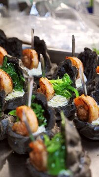 Chef decorating gourmet black tartlets with grilled shrimp, cream cheese, and chuka seaweed using tweezers