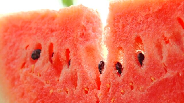 Watermelon slices reveal juicy red flesh and seeds, showcasing the vibrant interior in a bright, natural light setting