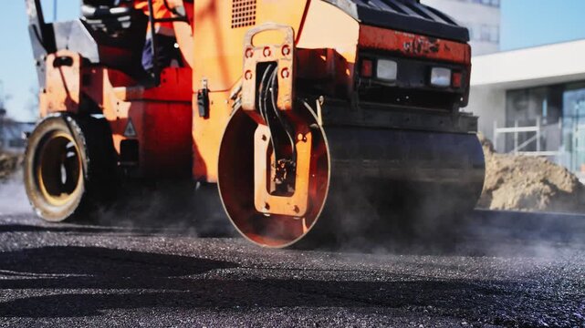 Road worker beside roller during fresh asphalt paving and compaction