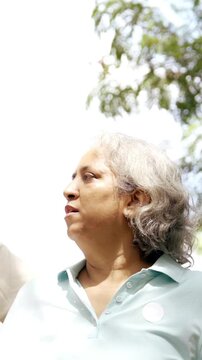 Indian Asian mid age couple in their fifties walking in the park, smiling and pointing, enjoying a pleasant conversation on a sunny day outdoors