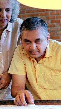 Indian Asian mid age couple in their fifties with gray hair playing carrom, enjoying an indoor board game with a light and happy mood