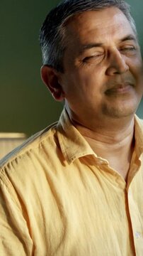 Indian Asian couple in their fifties with grey hair standing close by a large window, bathed in morning sunlight, both gazing outside with serious expressions, reflecting in the moment