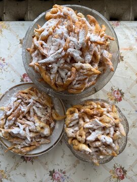 Angel wings pastry with powdered sugar on table. Traditional crispy deep fried sweet faworki chrust desserts inside plates on floral tablecloth for homemade baking food concept.