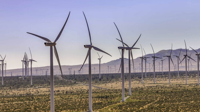 Aerial view of renewable energy landscape of modern utility scale wind turbines standing in the desert with arid terrain and clear blue sky in Palm Springs, California, United States.