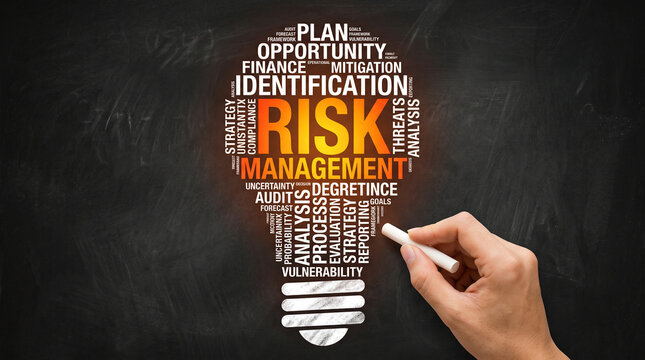 A lightbulb-shaped word cloud on a blackboard depicts risk management concepts, with a hand holding chalk, symbolizing planning and analysis, representing business strategy.