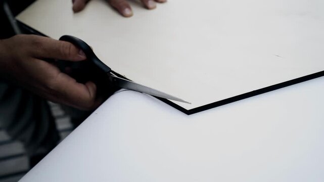 A man cuts a white sheet of paper with scissors. Close-up shooting
