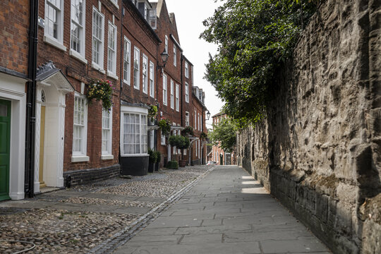 View of a historic cobblestone street lined with traditional red brick buildings and a weathered stone wall in Worcester, England, United Kingdom.