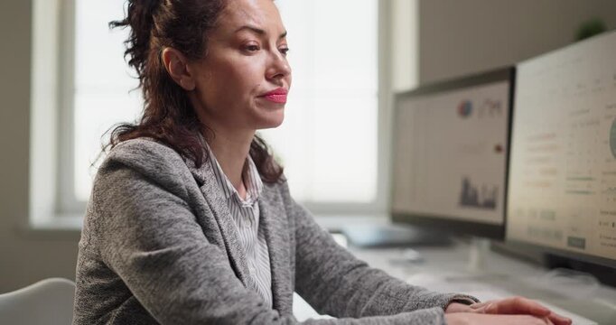 Woman employee in office at computer shows stress. She rubs her eyes, facing fatigue, headache and overwork as analyst reviewing complex finance charts. Clear office burnout stress concept.